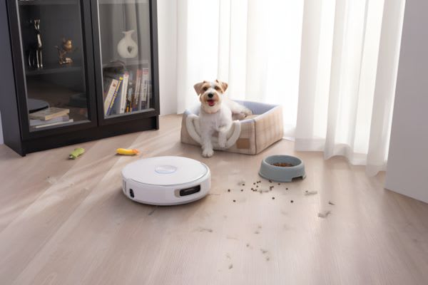 犬がいる部屋に自動掃除機があり、床には毛やおもちゃが散らばっています。家電 セールで最新モデルを手に入れましょう。