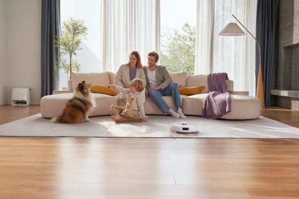 A family with a dog relaxes on a couch while a robot vacuum cleans up pet hair. Can Robot Vacuums Be Used for Pet Hair Removal?