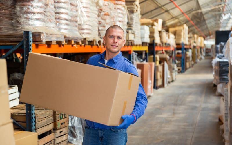 A warehouse worker carries a large box, showcasing the importance of IP rating in ensuring product safety during storage.