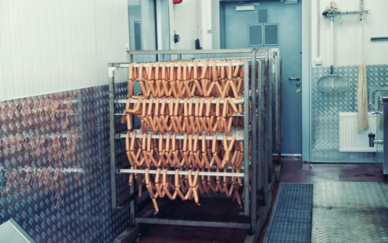 Sausages hanging on racks in a processing facility, showcasing an environment with specific hygiene standards and considerations for IP rating.