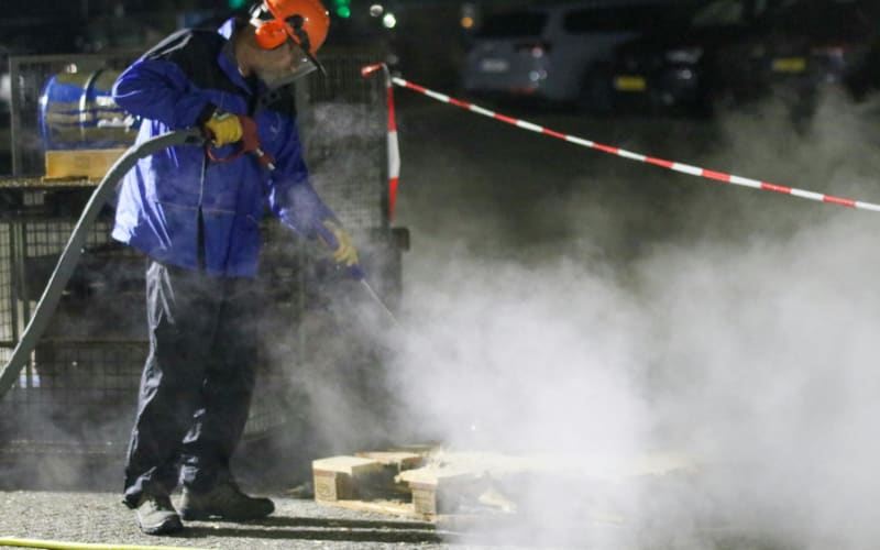 A worker in protective gear operates equipment, generating steam while ensuring safety with proper IP rating measures.