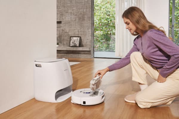 A woman demonstrates how to use a vacuum cleaner by emptying its dust bin into a storage base.