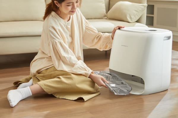 A woman sits on the floor, interacting with a robot vacuum, learning how to teach your robot vacuum to avoid obstacles.