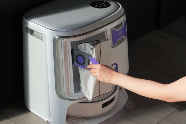 A hand demonstrates how to open vacuum cleaner dust bag on a modern vacuum cleaner unit.