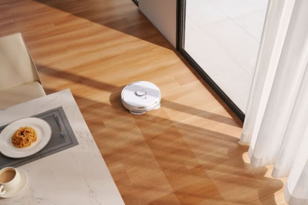 A robot vacuum cleans hardwood floors near a dining area, demonstrating how to use a robot vacuum for quick clean-ups.