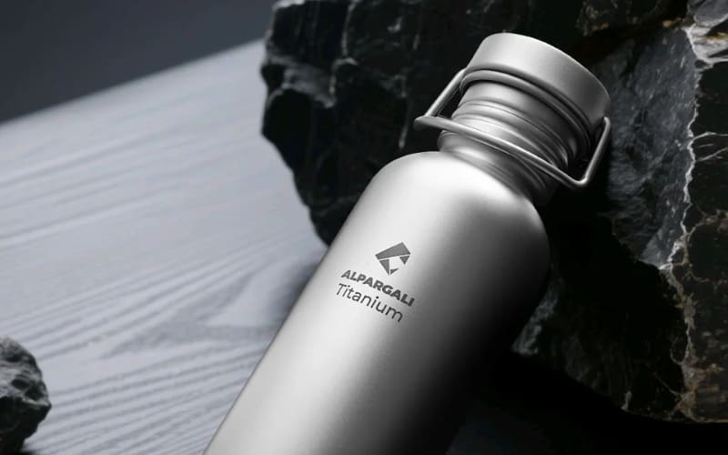 A sleek titanium water bottle resting on a rocky surface, ideal for hiking for beginners.