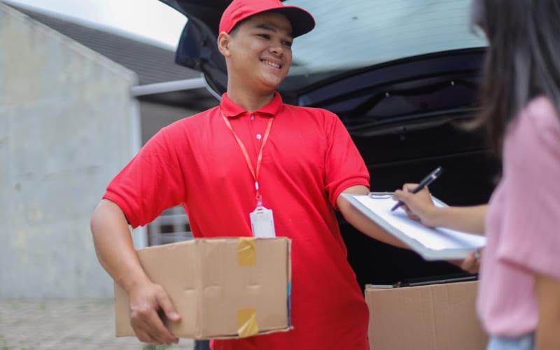 A delivery person in a red uniform hands over packages while using automatic identification and data capture for efficiency.