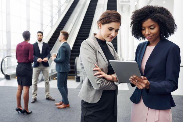 Two professionals discuss a home cleaning checklist while two others chat in a modern office lobby.