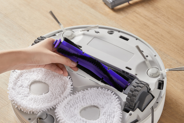 A person removing a beater bar from a robotic vacuum, illustrating what is a beater bar on a vacuum for cleaning purposes.