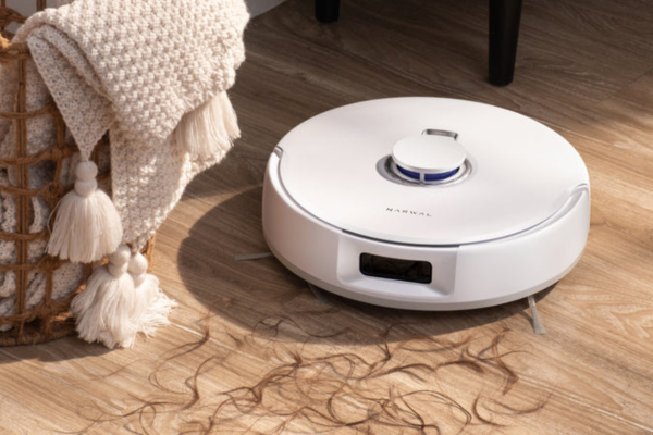 A robotic vacuum sits on wooden floors, surrounded by hair and a cozy blanket, raising questions like why is my vacuum spitting stuff back out?