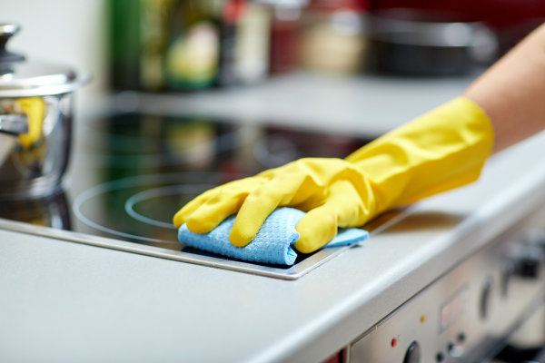 A hand wearing a yellow glove wipes the stovetop with a blue cloth during a spring clean up.