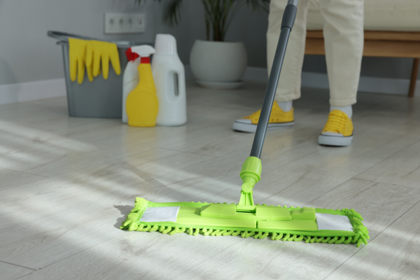 A person mops a wooden floor with a green mop, demonstrating how to mop effectively in a bright, clean space.