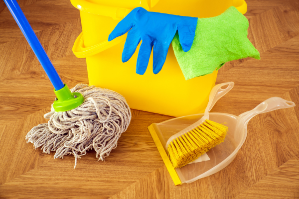 Cleaning supplies arranged on a wooden floor, including a mop, bucket, gloves, and dustpan, illustrating how to mop effectively.