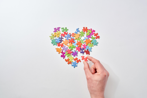 A hand picks up a puzzle piece among colorful pieces arranged in a heart shape, perfect for Valentine's Day gifts.