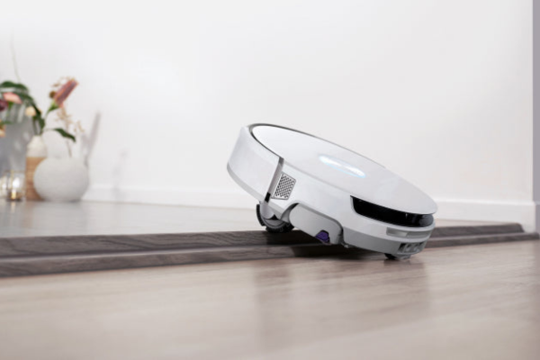 A robotic vacuum cleaner smoothly transitions from a wooden floor to a rug, showcasing the best lightweight vacuum design.