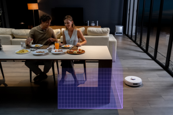 A couple enjoys a meal at a dining table while the best budget robot vacuum with mapping cleans the floor nearby.