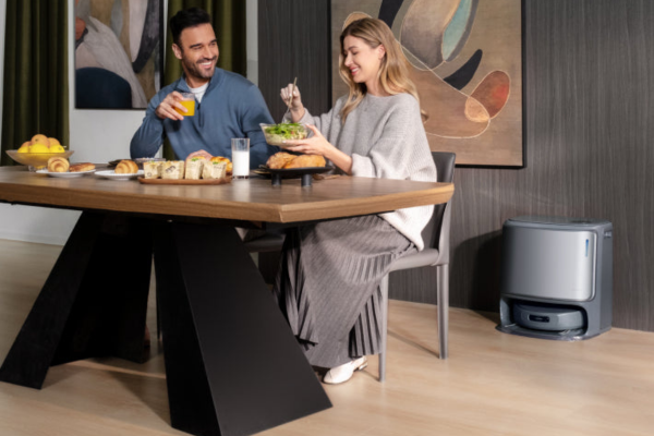 A couple enjoys breakfast at a table, while the best automatic vacuum quietly cleans nearby, enhancing their relaxing moment.