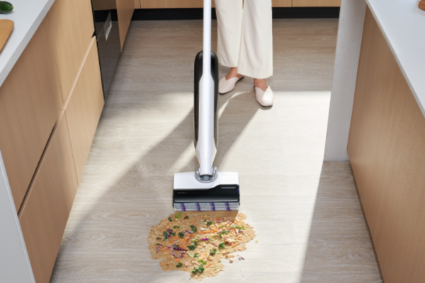 A person using the best anti hair wrap vacuum to clean up a mess on the kitchen floor, showcasing its efficiency and design.