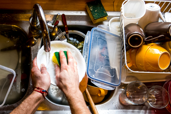 Hands washing dishes in a sink filled with soapy water, showcasing the effort of cleaning after a party.