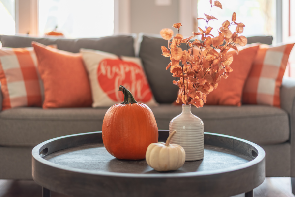 A cozy living room with orange pillows, decorative pumpkins, and a floral arrangement, perfect for cleaning after a party.