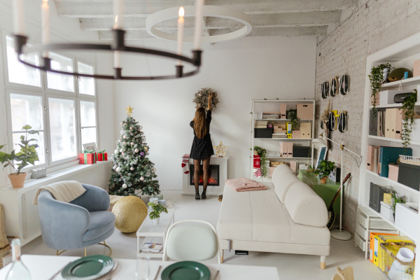 A woman decorates a wall while cleaning after a party in a cozy room with a Christmas tree and modern furniture.
