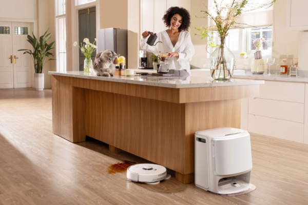 A woman prepares food in a kitchen with a cat nearby and a robotic vacuum mop, ideal for cleaning hardwood floors.