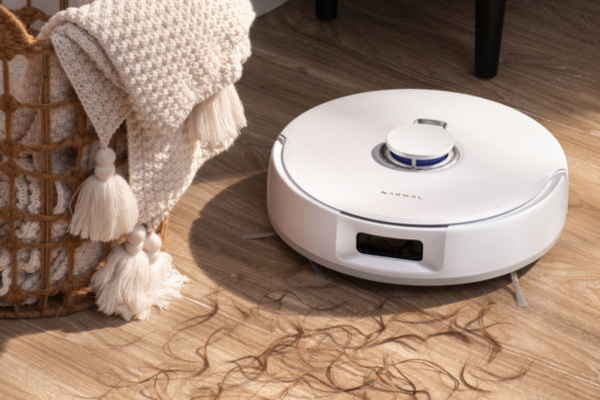 A robotic vacuum on wooden floors, efficiently picking up hair, ideal for a hair salon setting as the best vacuum for hair salon.