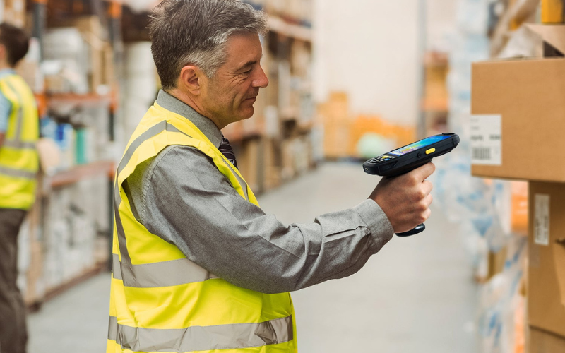 A worker in a warehouse uses a barcode scanner, showcasing impressive barcode scanner speed while managing inventory.