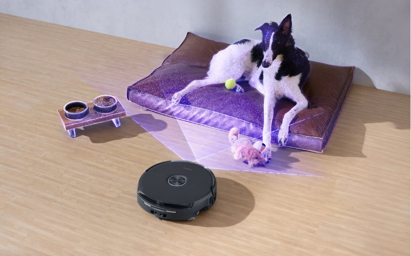 A dog relaxes on a bed while a robot vacuum navigates around, showcasing the narwal flow 2 vs flow innovation in cleaning.