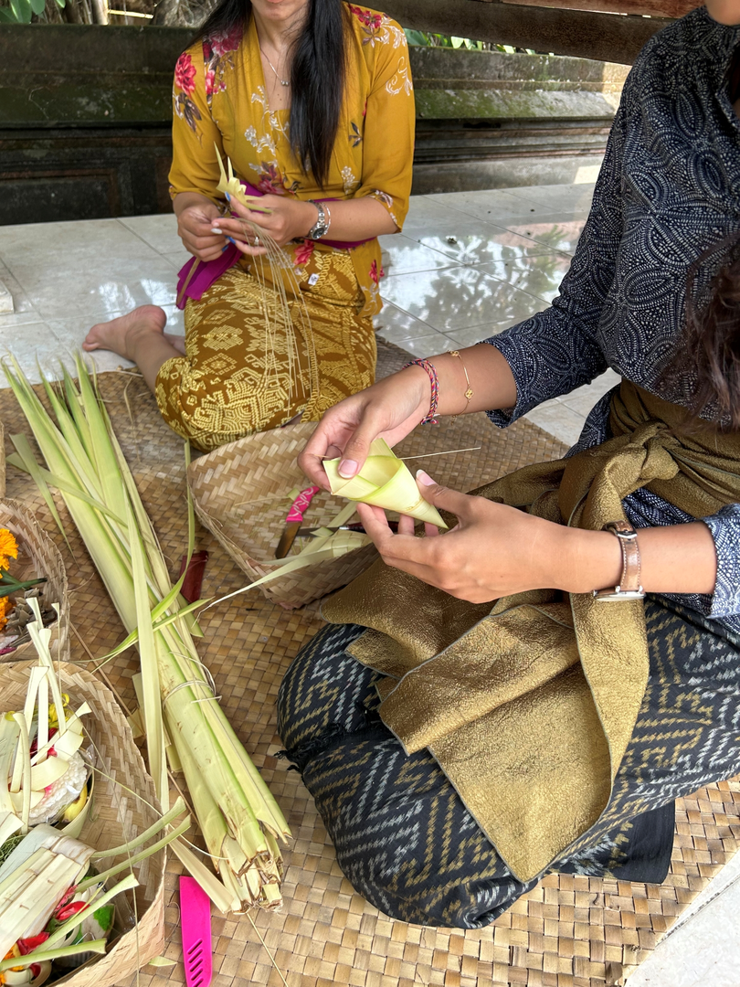 As the activity continues, participants learn to make Balinese offerings by folding palm leaves and preparing traditional canang sari as part of a cultural class in Bali.