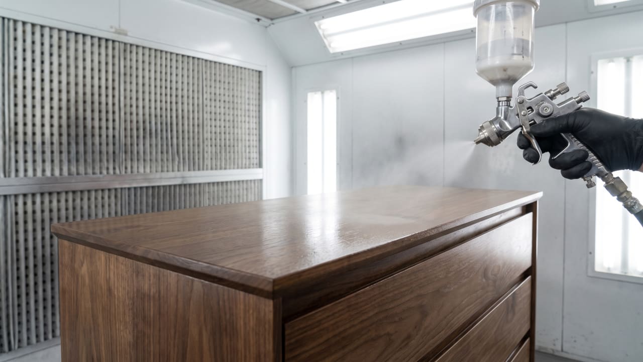 Wood furniture piece being sprayed with a clear lacquer finish in a professional spray booth