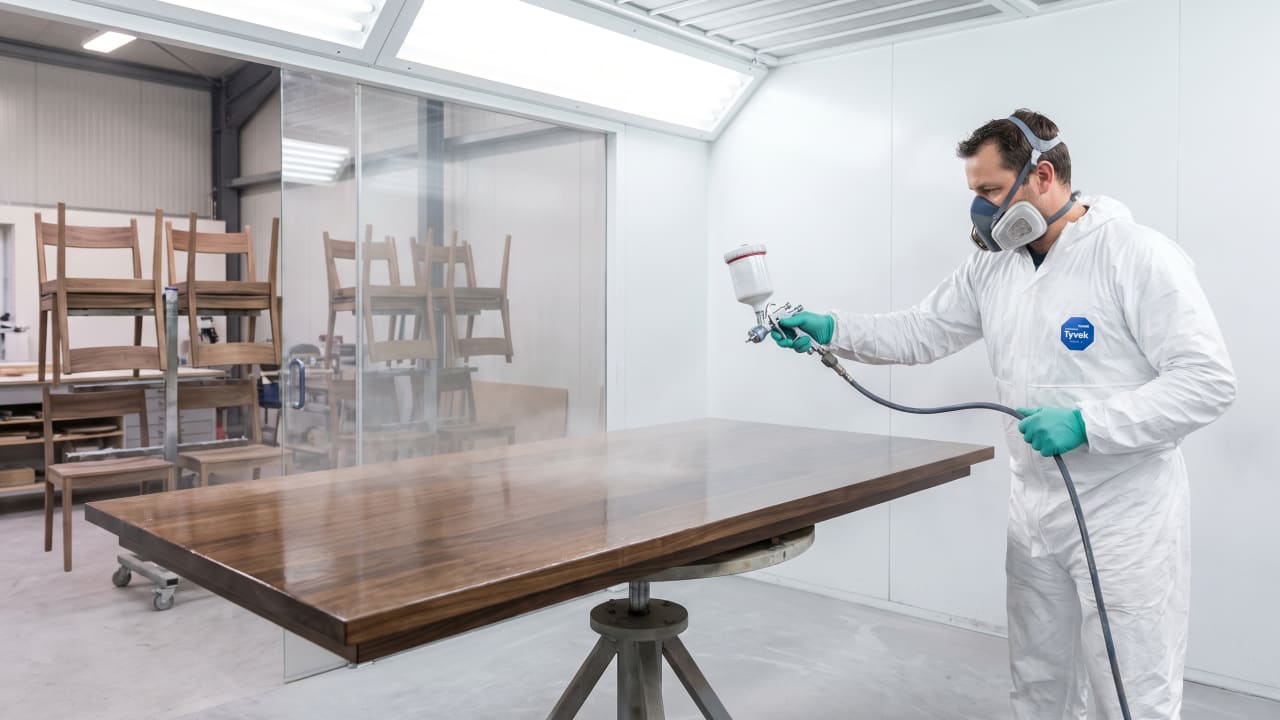 Craftsman applying a lacquer topcoat to a dining table in the shop