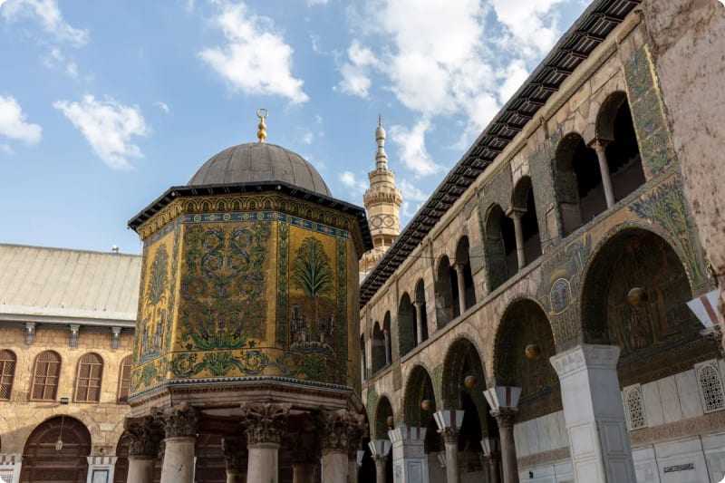 The ornate Dome of the Rock with intricate mosaics, surrounded by arches and a minaret, set against a blue sky.