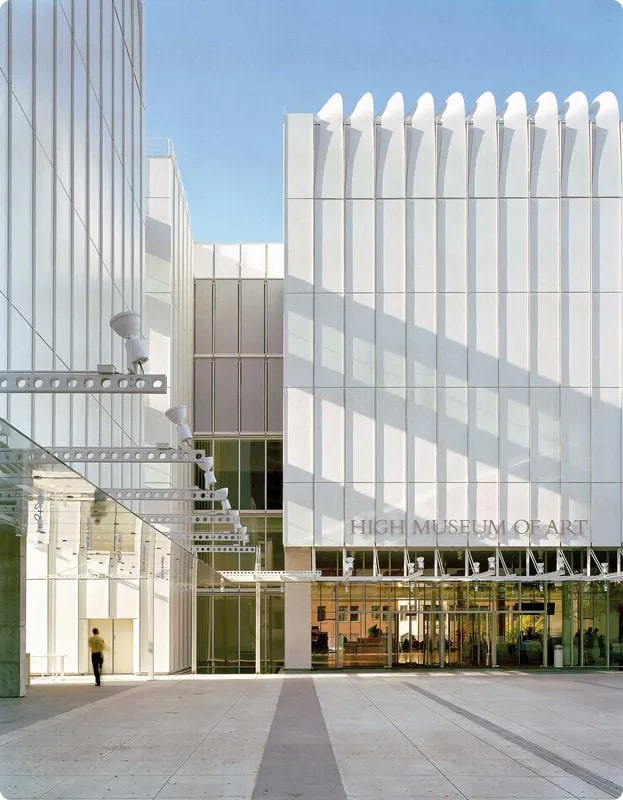 Exterior view of the High Museum of Art, featuring modern architecture with white panels and large glass windows under a clear blue sky.