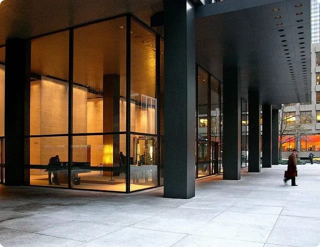 Modern building exterior featuring large glass windows and a sleek black overhang, with people walking by.