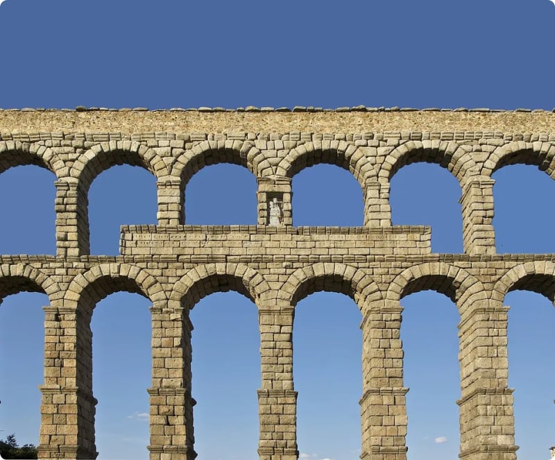 Ancient stone aqueduct with multiple arches against a clear blue sky.