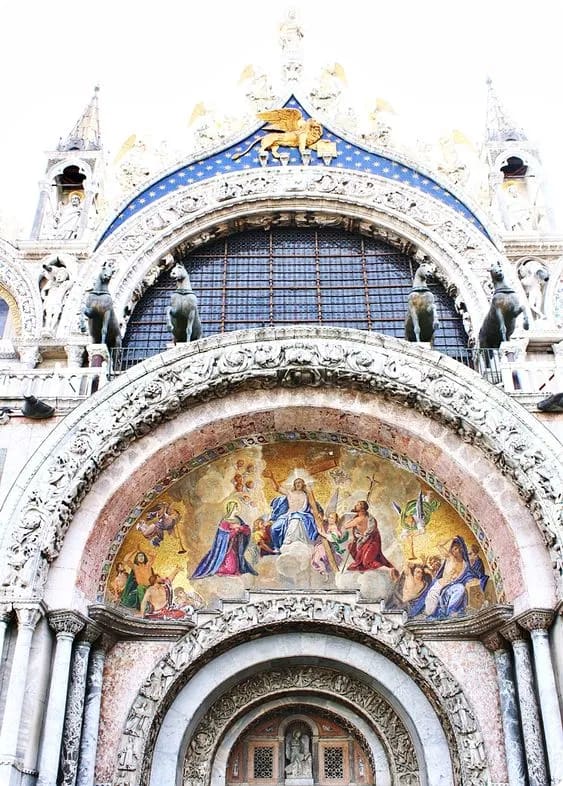 Facade of St. Mark's Basilica in Venice, featuring intricate mosaics and sculptures, including a prominent golden winged lion at the top.
