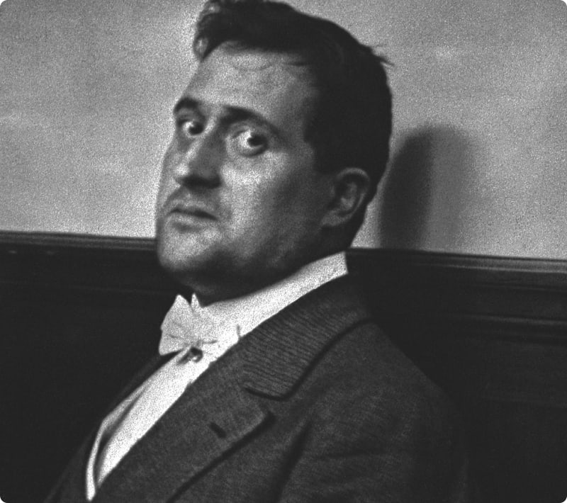 A black and white portrait of a man in formal attire, looking over his shoulder with a serious expression.