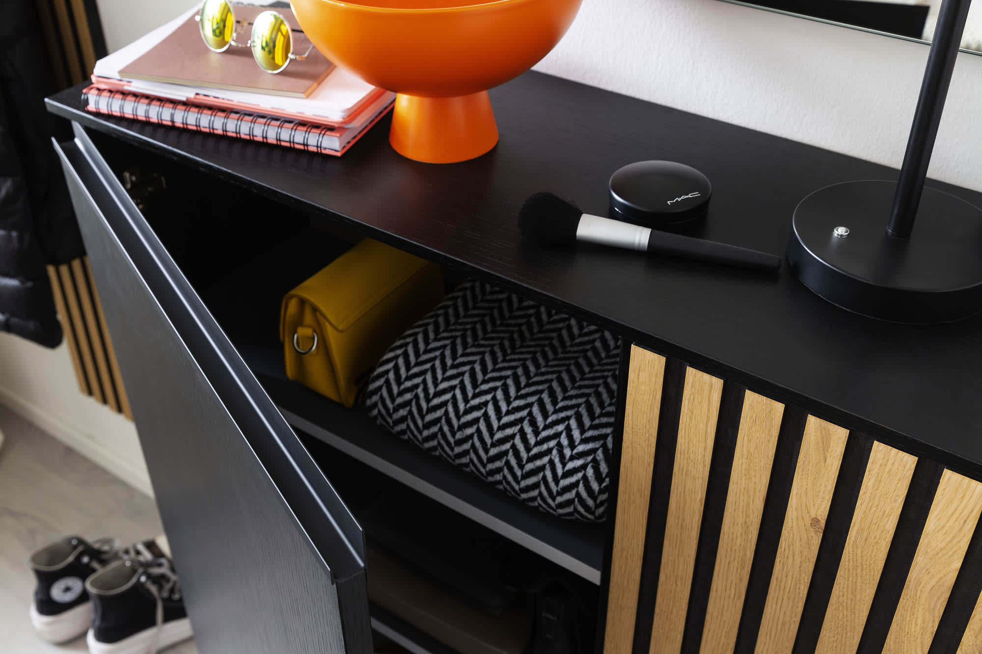 Die Garderobe Punta, ein schwarzer Schrank mit Holzakzenten, ist teilweise geöffnet und gibt den Blick auf eine Decke und eine gelbe Tasche frei, die darin aufbewahrt werden. Die Garderobe Punta, ein schwarzer Schrank mit Holzakzenten, ist teilweise geöffnet und gibt den Blick auf eine Decke und eine gelbe Tasche frei, die darin aufbewahrt werden.