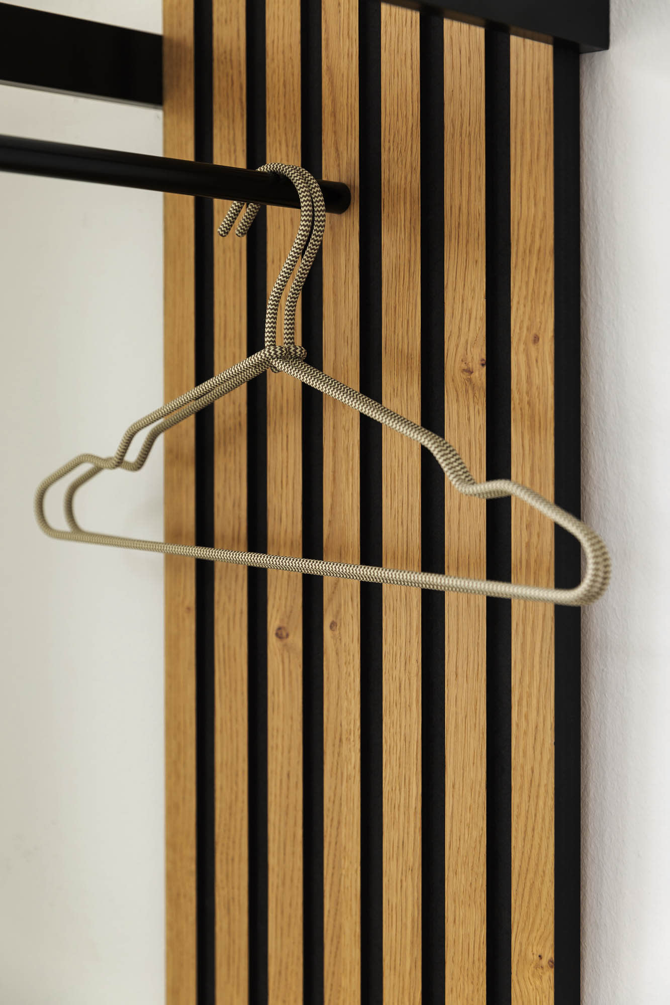 Der Metallbügel Garderobe Punta hängt an einer schwarzen Stange, die an einer Holzlattenwand befestigt ist. Der Metallbügel Garderobe Punta hängt an einer schwarzen Stange, die an einer Holzlattenwand befestigt ist.