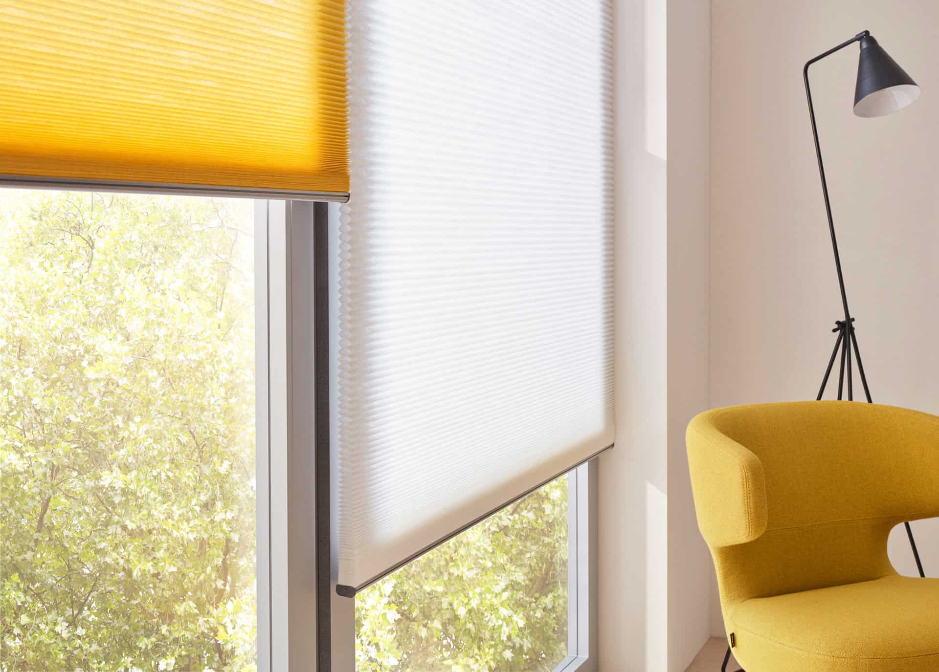 Chambre moderne avec de grandes fenêtres, des stores jaunes et blancs, une chaise jaune et un lampadaire noir.
