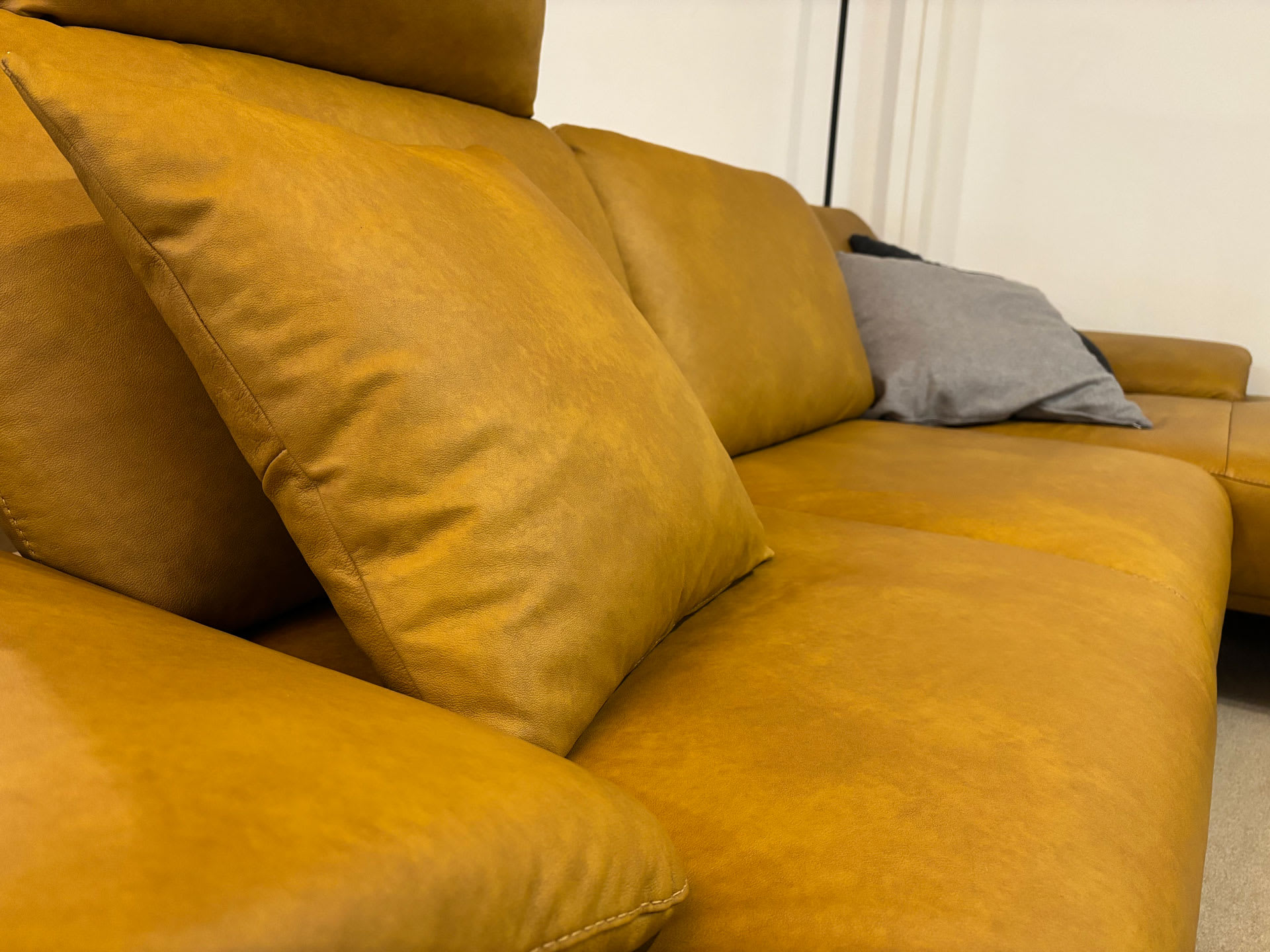 Nahaufnahme des senfgelben Sofas „Polstergruppe Samiraa“ mit Plüschkissen, darunter ein graues, vor einer weißen Wand. Nahaufnahme des senfgelben Sofas „Polstergruppe Samiraa“ mit Plüschkissen, darunter ein graues, vor einer weißen Wand.