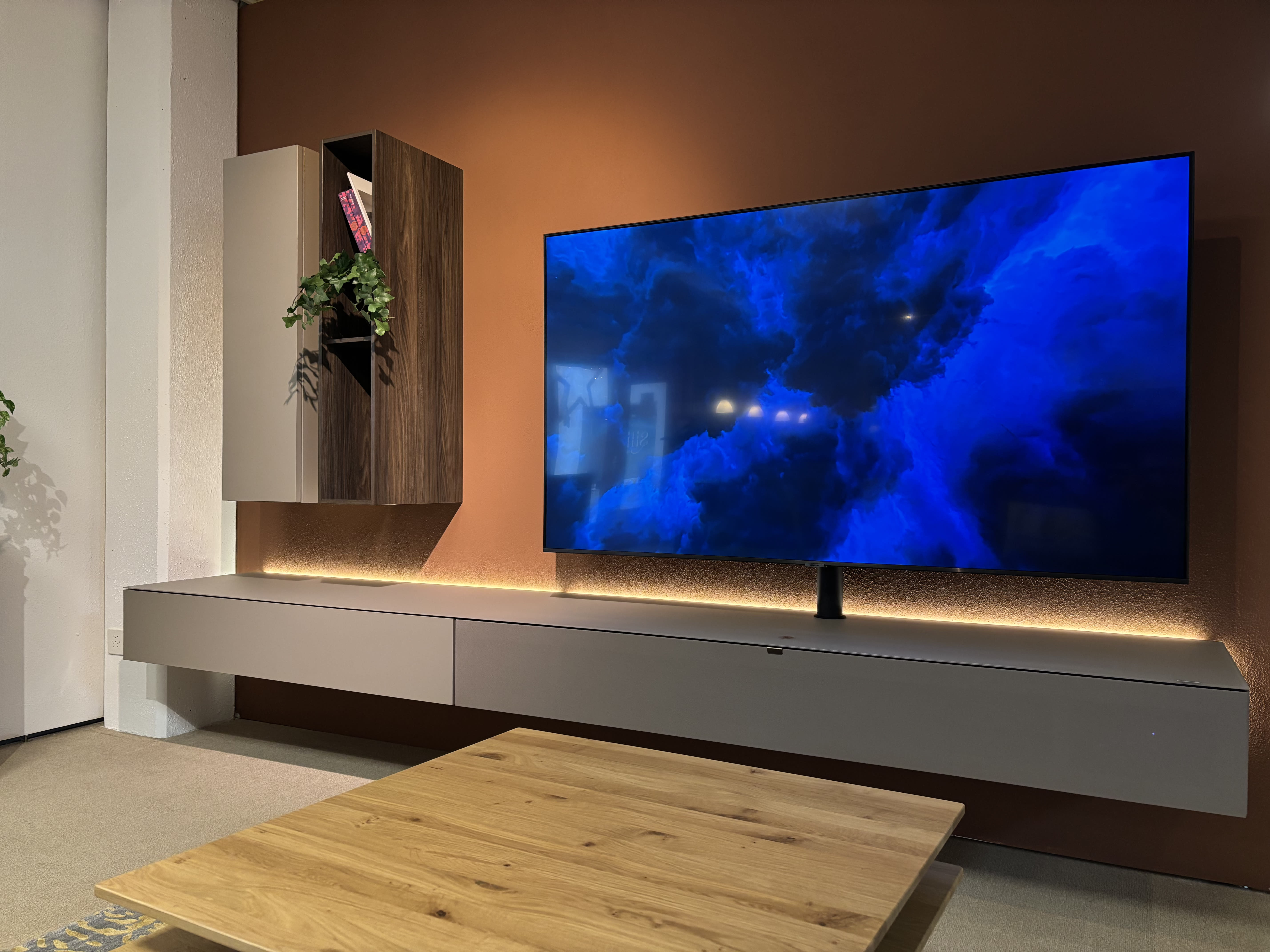 Modernes Wohnzimmer mit einem wandmontierten TV-Gerät auf dem TV-Möbel Next von Spectral, schwebenden Regalen und einem Couchtisch aus Holz.
