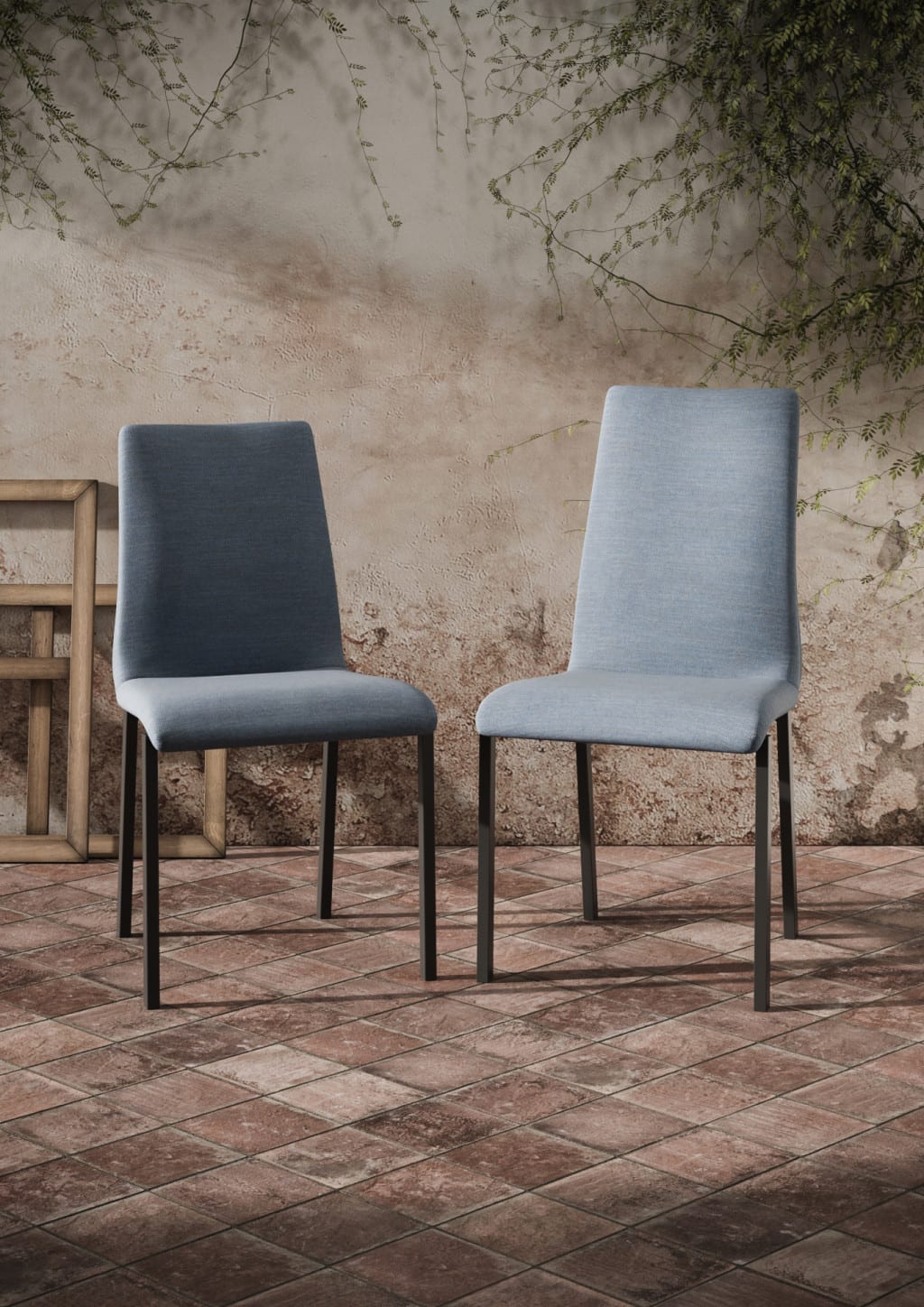Zwei Willisau Stuhl Leni, blau gepolstert und mit schwarzen Beinen, stehen auf einem gefliesten Boden vor einer rustikalen Wand mit Ranken. Zwei Willisau Stuhl Leni, blau gepolstert und mit schwarzen Beinen, stehen auf einem gefliesten Boden vor einer rustikalen Wand mit Ranken.