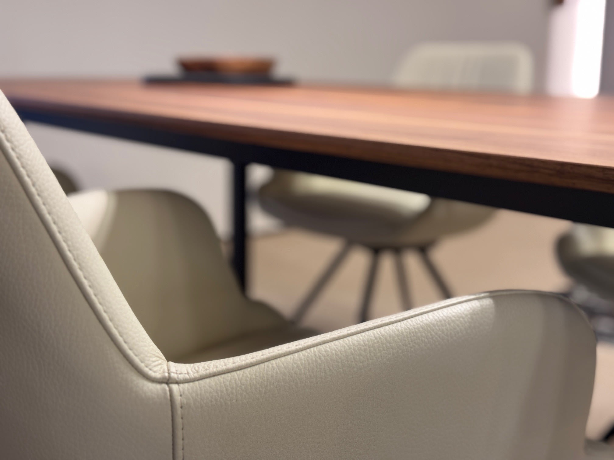 Nahaufnahme eines Willisau Stuhl Loreo in Beige neben einem Holztisch, mit unscharfen Stühlen und einer Schüssel im Hintergrund. Nahaufnahme eines Willisau Stuhl Loreo in Beige neben einem Holztisch, mit unscharfen Stühlen und einer Schüssel im Hintergrund.