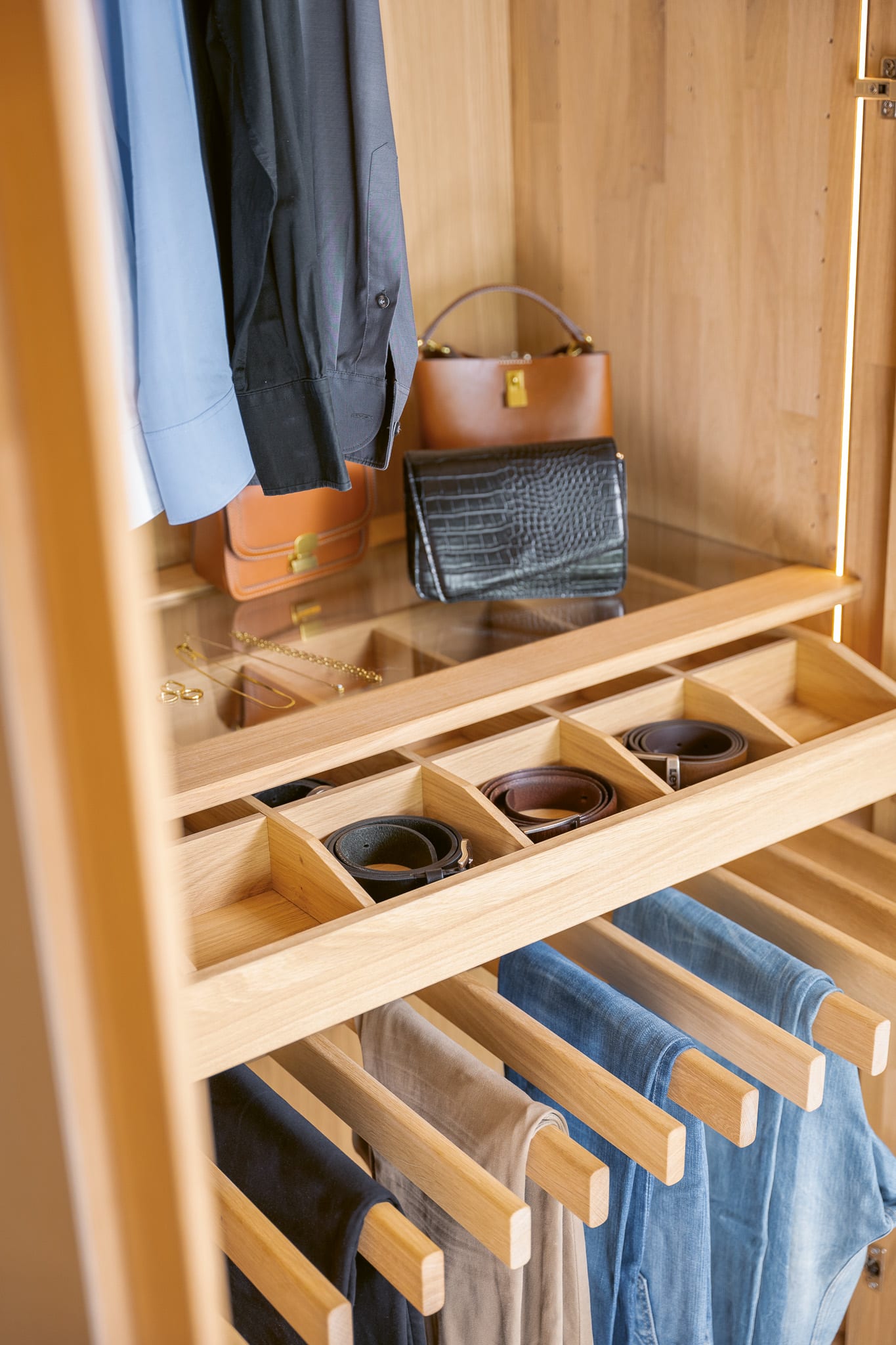 Ein übersichtlicher Kleiderschrank mit hängenden Kleidern, Gürteln in einer Schublade und Handtaschen in einem Regal ergänzt das Wimmer Bett Silvan. Ein übersichtlicher Kleiderschrank mit hängenden Kleidern, Gürteln in einer Schublade und Handtaschen in einem Regal ergänzt das Wimmer Bett Silvan.