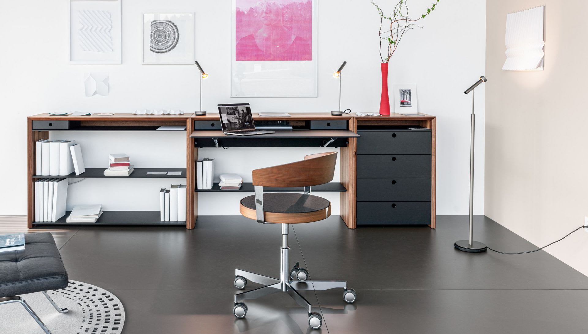 Modernes, minimalistisches Büro mit dem Girsberger Sideboard LaPunt, einem Holzschreibtisch, Drehstuhl, Laptop, Büchern, Wandkunst und einer hohen Vase mit Zweigen. Modernes, minimalistisches Büro mit dem Girsberger Sideboard LaPunt, einem Holzschreibtisch, Drehstuhl, Laptop, Büchern, Wandkunst und einer hohen Vase mit Zweigen.