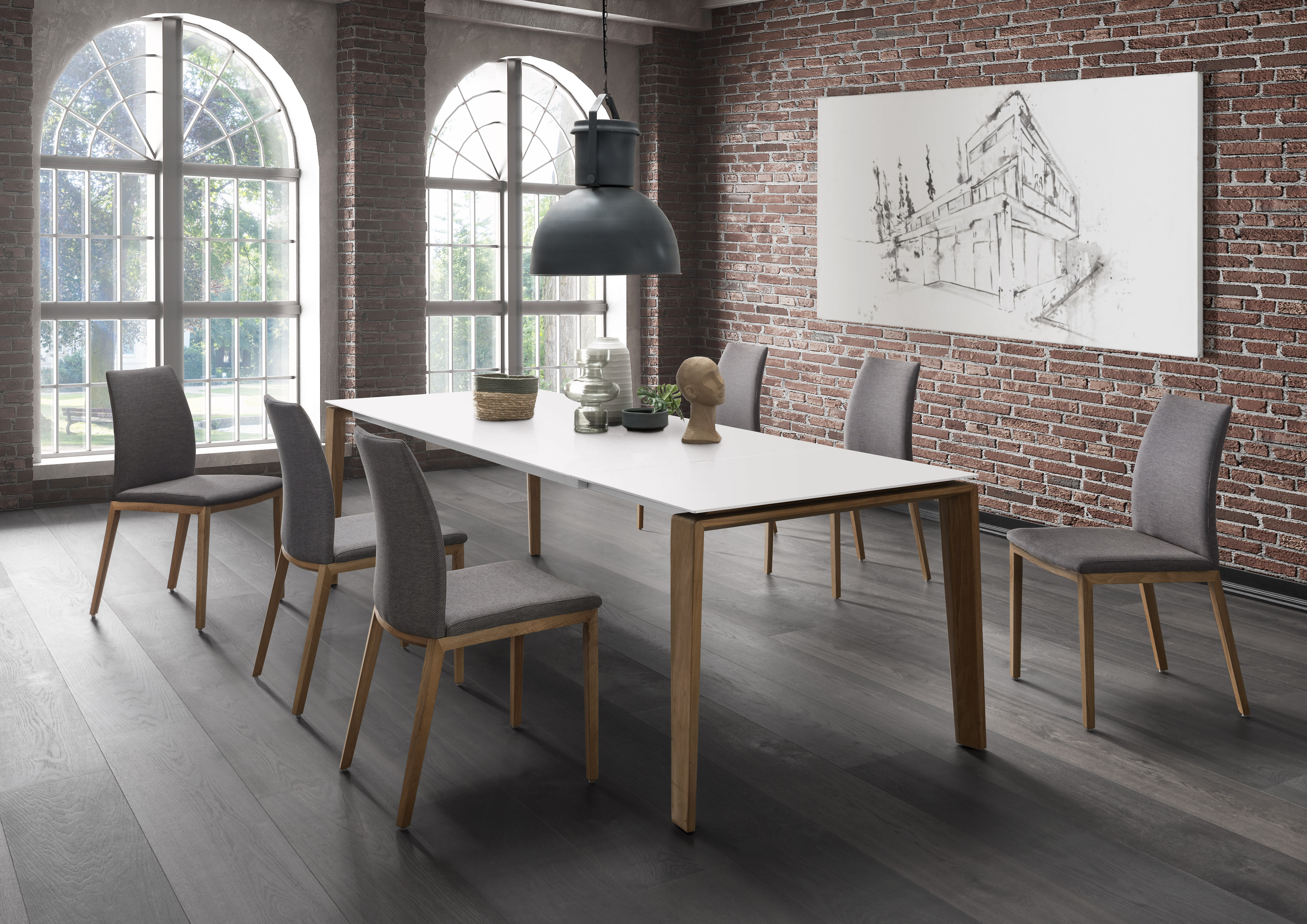 Modernes Esszimmer mit dem Sit Mobilia Tisch Olympia Turin, sechs Stühlen, Backsteinwänden, großen Fenstern und einem skizzenhaften Kunstwerk.