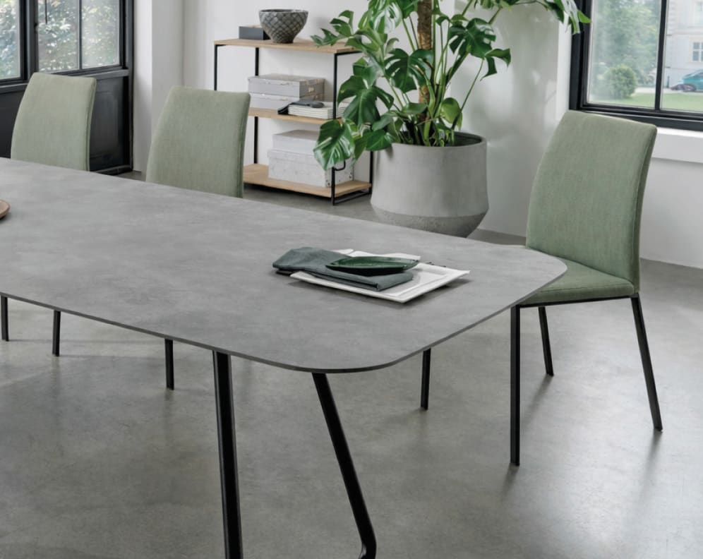 Modernes Esszimmer mit einem grauen Tisch, Sit Mobilia Stuhl Fedora grün, einer Topfpflanze und einem Regal mit Büchern am Fenster. Modernes Esszimmer mit einem grauen Tisch, Sit Mobilia Stuhl Fedora grün, einer Topfpflanze und einem Regal mit Büchern am Fenster.