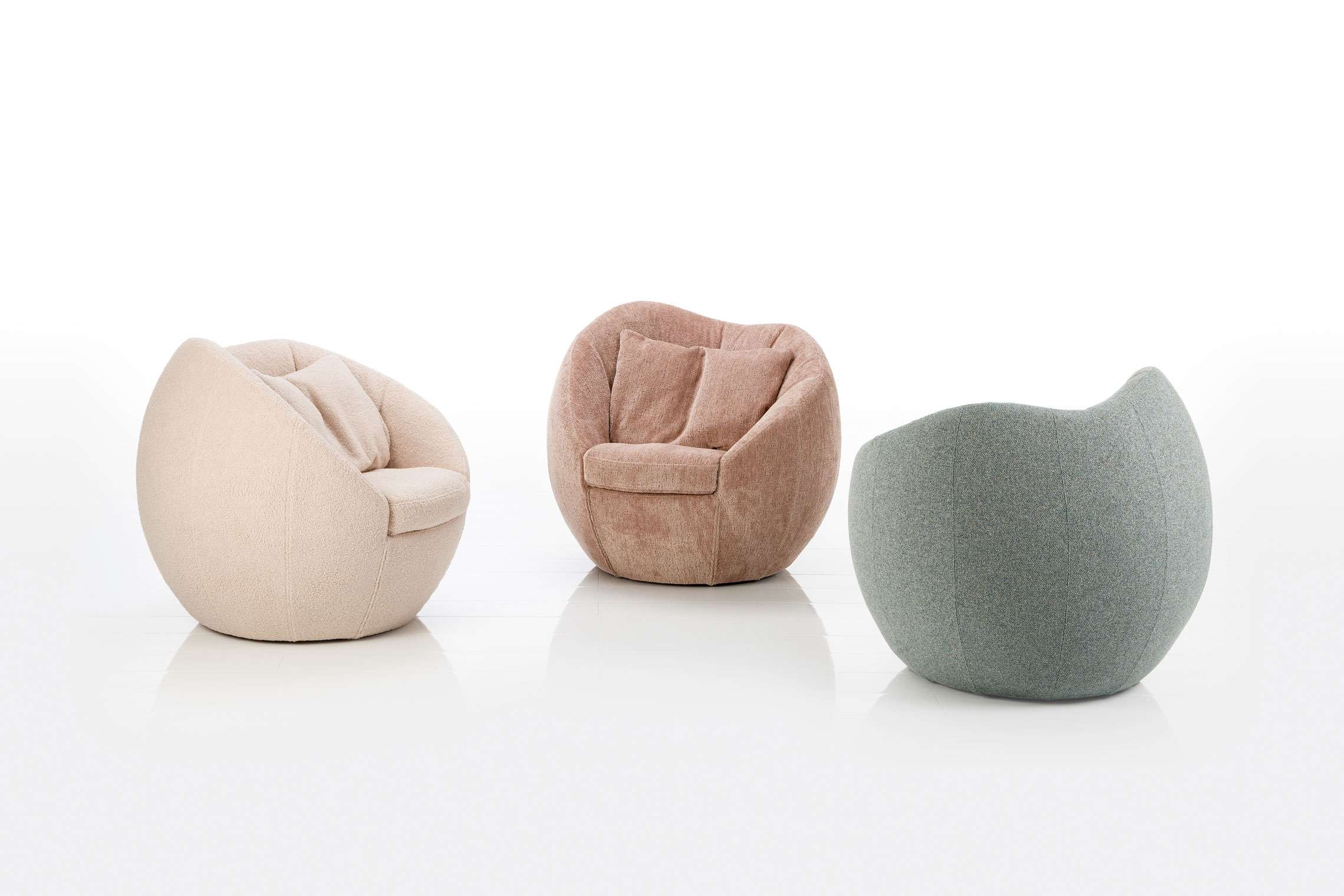 Drei runde, gepolsterte Brühl Sessel Azur Lounge Chairs in Beige, Rosa und Grün stehen auf weißem Grund. Drei runde, gepolsterte Brühl Sessel Azur Lounge Chairs in Beige, Rosa und Grün stehen auf weißem Grund.